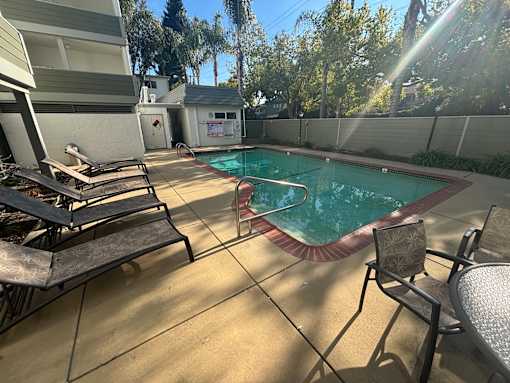 A pool surrounded by chairs and trees.