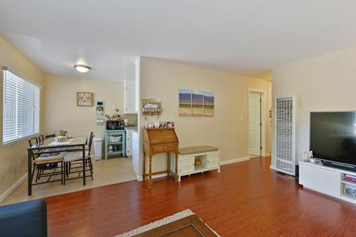 A living room with a wooden floor and a dining table with chairs.