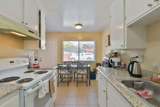 A kitchen with a white stove top oven and white cabinets.