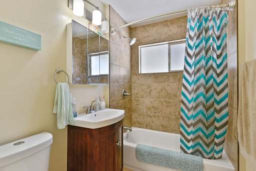 A bathroom with a white bathtub, a sink, a mirror, and a shower curtain.