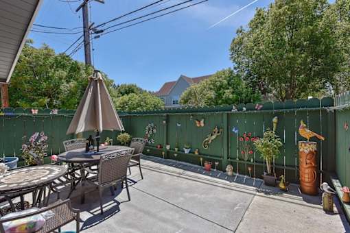 A patio with a table and chairs and a green fence.