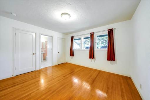 a living room with a hard wood floor and a window with red curtains