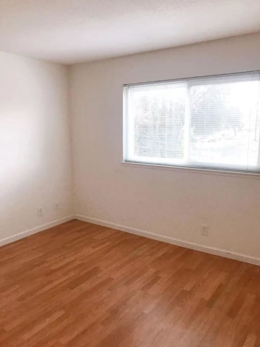 an empty room with a window and wooden floors