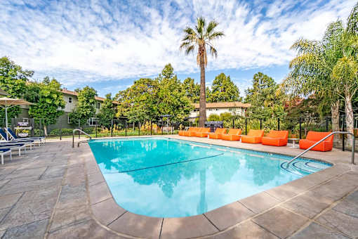 a swimming pool with orange chairs and a palm tree