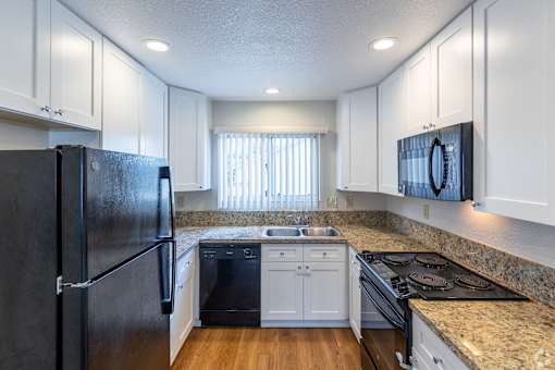 a kitchen with white cabinets and granite counter tops and a black refrigerator