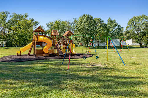 A playground with a yellow slide and a green swing set.