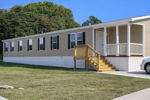 A mobile home with a porch and a car parked in front.