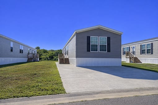 A house with a grey siding and a white trim is surrounded by a grassy area and other similar houses.