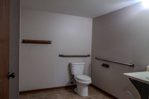 A white toilet sits in a small bathroom with a white sink and a towel bar.