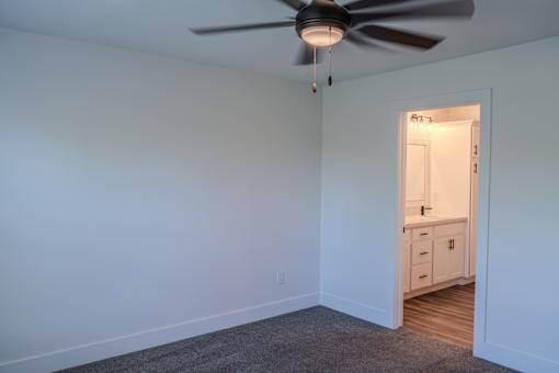 A room with a ceiling fan and a doorway leading to a bathroom.