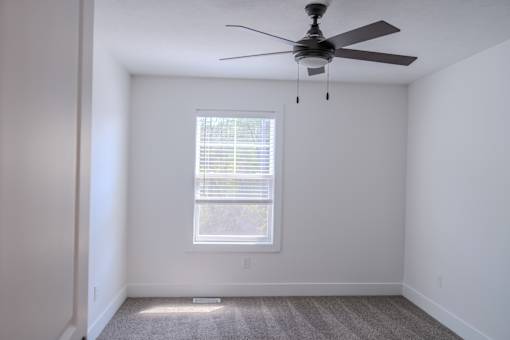 A room with a ceiling fan and a window with blinds.