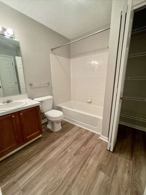 A white toilet sits in a bathroom with wood flooring and a walk-in shower.