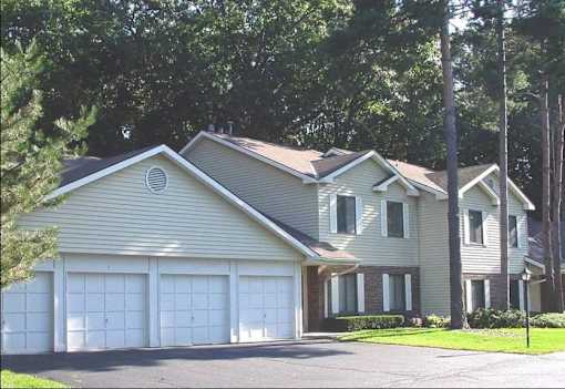 A two-story house with a garage is surrounded by trees.