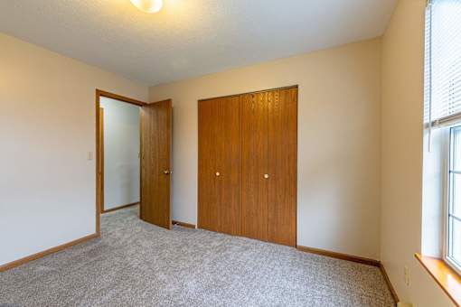 A room with a carpeted floor, two wooden doors, and a window with blinds.