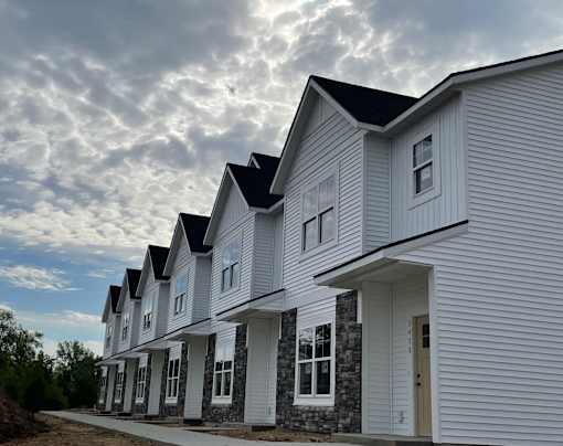 A row of new houses with white siding and dark roofs at The Vue at Rivertown Park Townhomes, Michigan