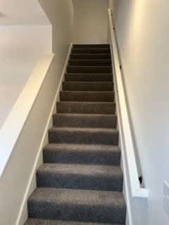 A staircase with a grey carpeted runner and white risers at The Vue at Rivertown Park Townhomes, Michigan