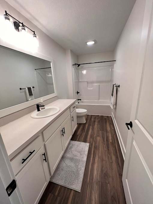 A bathroom with a sink, mirror, toilet, and wooden floors at The Vue at Rivertown Park Townhomes, Wyoming  