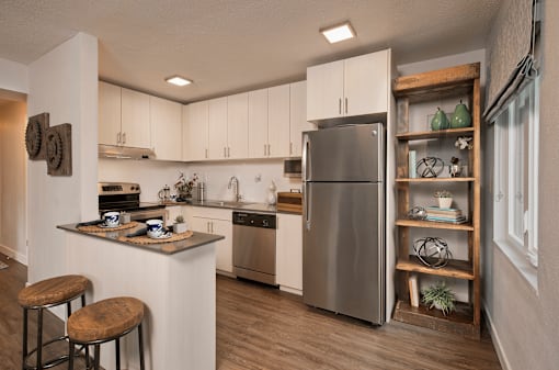 A modern kitchen with a stainless steel refrigerator and wooden bar stools