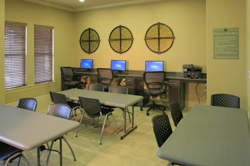 A room with tables and chairs and computers on the wall.