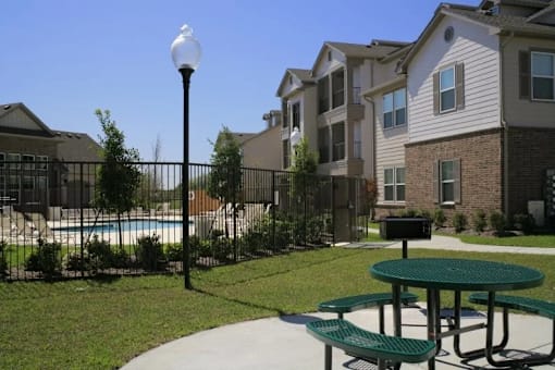 A green picnic table sits in the middle of a grassy area in front of apartment buildings.