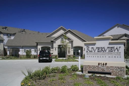 A black car is parked in front of a building with a sign that says "Riverview Apartment Homes #144".