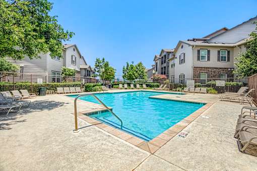 A swimming pool surrounded by lounge chairs and trees in a residential area.