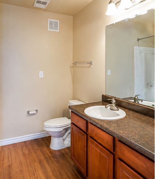A bathroom with a toilet, sink, mirror, and a towel bar.