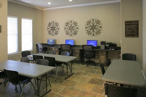 A room with tables and chairs and computers on desks.
