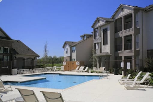 A swimming pool surrounded by lounge chairs in front of apartment buildings.