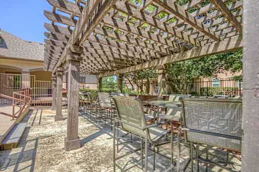 A patio with a wooden pergola and metal chairs.