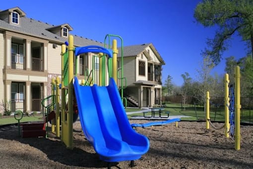 A blue slide in a playground with a building in the background.