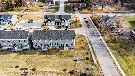 A large building with a grey roof is surrounded by smaller buildings and trees.