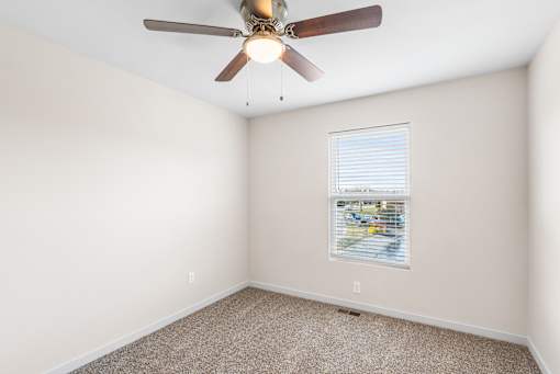 A room with a ceiling fan and a window with blinds.