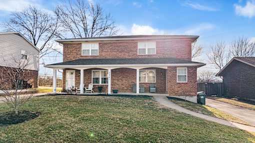 A house with a brick facade and a green trash can in front.