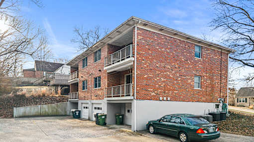 A green car is parked in front of a red brick house.