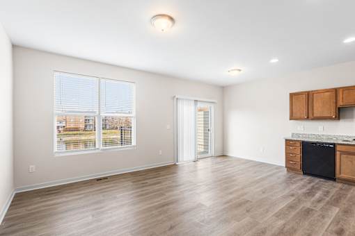 A spacious room with wooden flooring and a kitchen area with cabinets and a dishwasher.