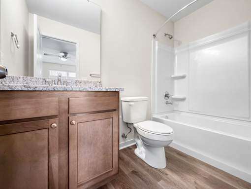 A white toilet sits in a bathroom with a wooden cabinet and a white bathtub.