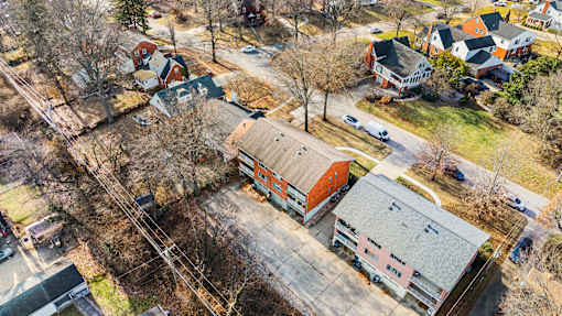 A large building with a red roof is surrounded by smaller buildings and trees.