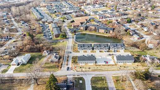A bird's eye view of a residential area with a large building and a pond.