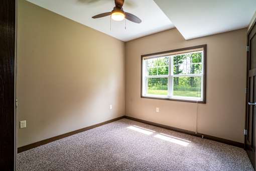 A room with a ceiling fan and a window showing greenery outside.