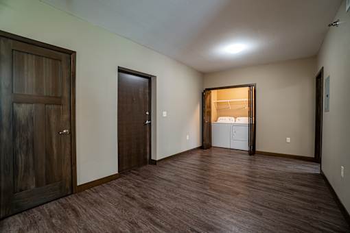 A room with brown flooring and a white fridge in the corner.