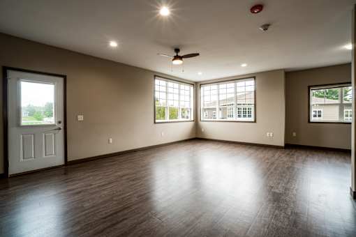 A room with a ceiling fan and large windows.
