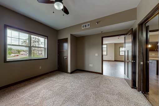 A room with a carpet floor, a ceiling fan, and a large window.