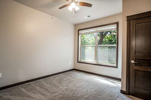 A room with a ceiling fan and a window showing trees outside.