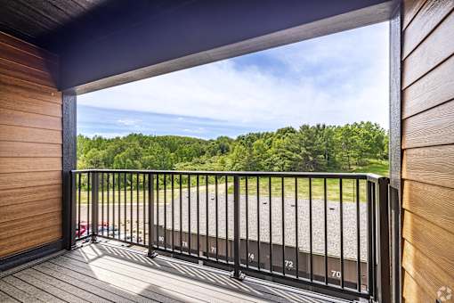 A balcony with a black railing and a view of a parking lot and trees.