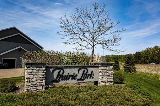 A sign that says Prairie Park in front of a house and a tree.