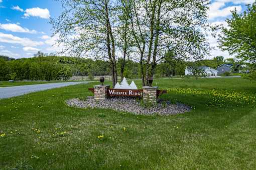 A sign that says Whisper Ridge is in the middle of a grassy area.
