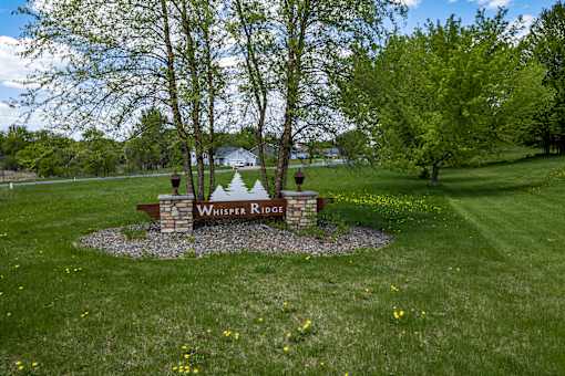 A sign that says Whisper Ridge is in the middle of a grassy area.