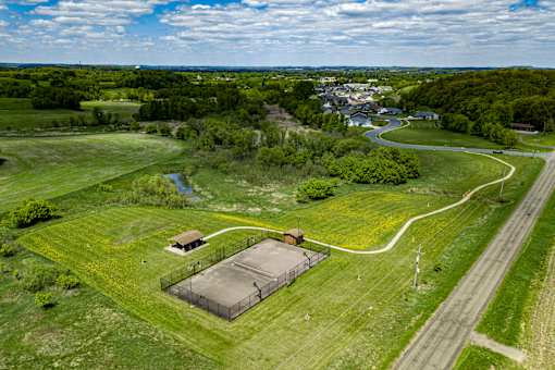 A small building sits in a grassy field with a road and trees in the background.