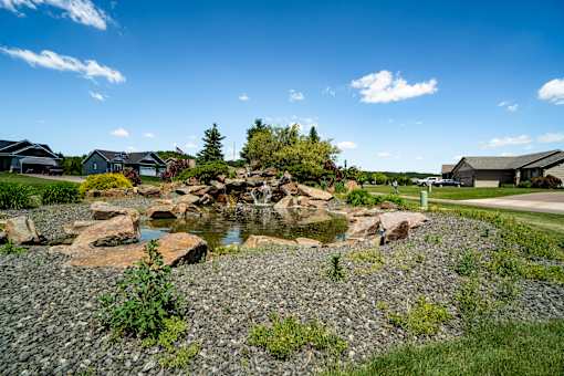 A small pond with rocks in the foreground and houses in the background.
